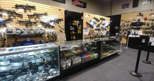 A display of firearms and accessories in a retail store, featuring glass cases and wall-mounted racks.