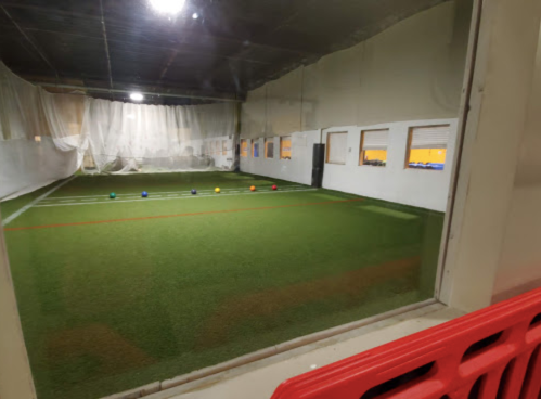 Indoor sports facility with artificial turf, featuring colorful balls lined up on the field and large windows.