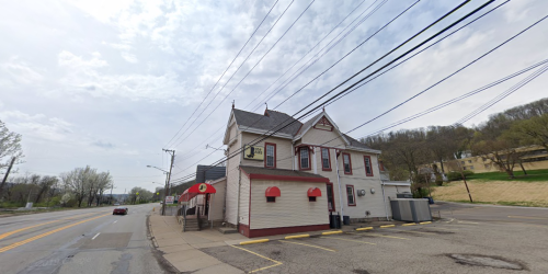 A two-story building with a red awning, located on a street with power lines and greenery in the background.