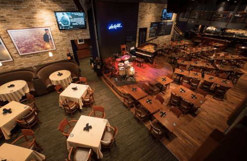 A spacious restaurant with wooden tables, a stage for live music, and a cozy atmosphere.