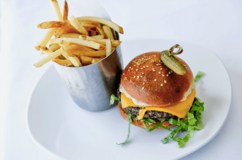 A juicy cheeseburger with lettuce and a pickle, served with a side of crispy French fries on a white plate.