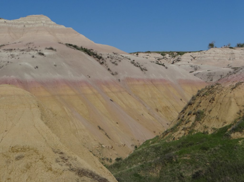 Colorful layered hills under a clear blue sky, showcasing shades of yellow, pink, and beige in a natural landscape.