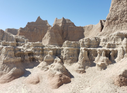 Rocky formations and eroded cliffs under a clear blue sky in a desert landscape.