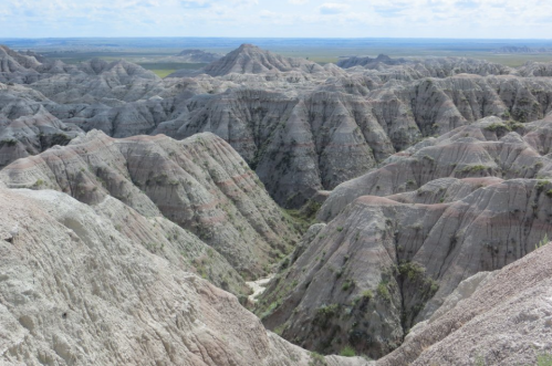 A panoramic view of rugged, layered rock formations in a vast, open landscape under a cloudy sky.