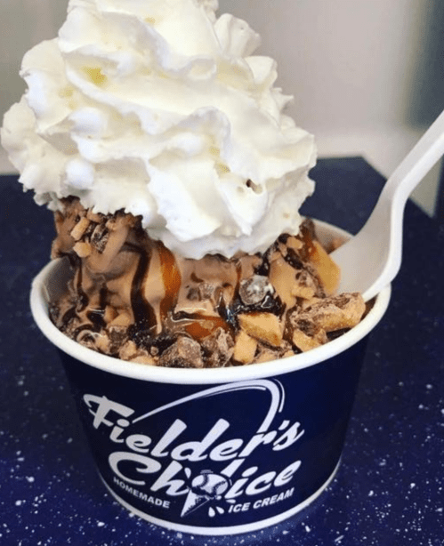 A cup of ice cream topped with whipped cream, chocolate sauce, and crushed candy, labeled "Fielder's Choice."