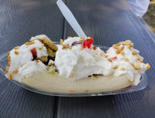 A banana split topped with whipped cream, nuts, and cherries, served in a clear dish on a wooden table.