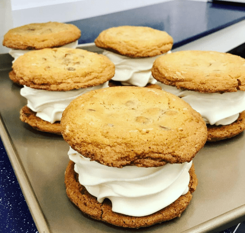 Six cookie sandwiches filled with creamy white frosting, arranged on a baking tray.