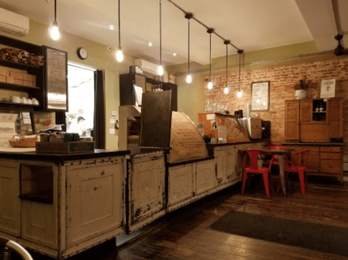 Cozy café interior with rustic decor, wooden counters, red chairs, and warm lighting.