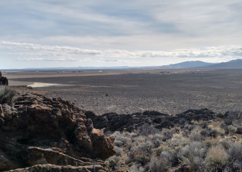A vast, arid landscape with rocky terrain, sparse vegetation, and distant mountains under a cloudy sky.