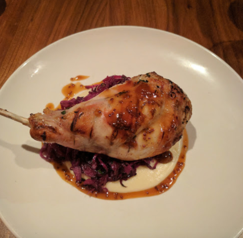 A roasted chicken leg on a bed of purple cabbage with a savory sauce, served on a white plate.