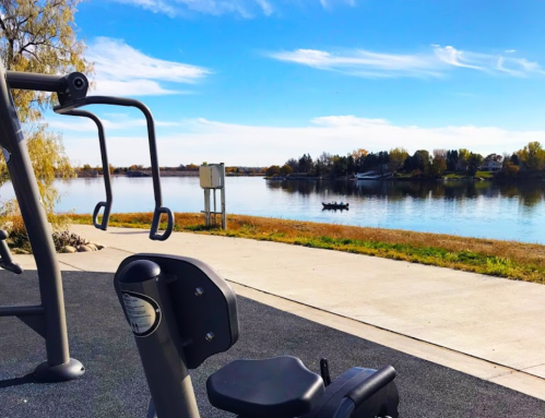 Outdoor gym equipment in the foreground with a calm lake and blue sky in the background.