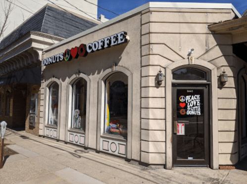 A charming donut shop with a coffee sign, featuring large windows and a colorful "Peace, Love & Donuts" message on the door.