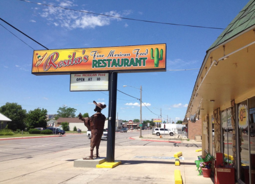 Sign for Rosita's Fine Mexican Food Restaurant, featuring a cowboy statue and a bright blue sky in the background.