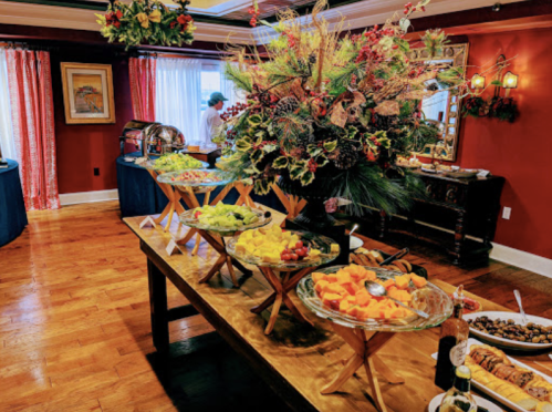 A festive dining room with a table of colorful fruit platters and holiday decorations in the background.