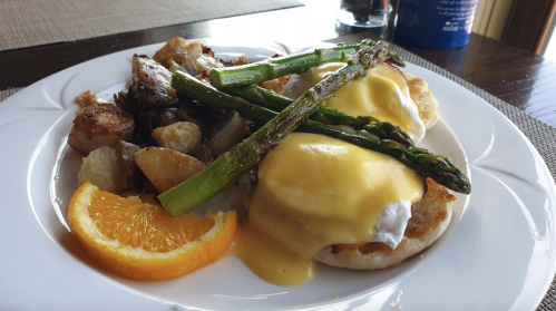 A plate of eggs Benedict with asparagus, roasted potatoes, and a slice of orange on the side.