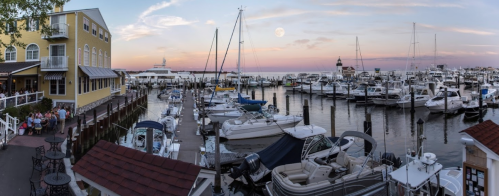 A scenic marina at sunset, featuring boats docked and a vibrant sky with a full moon rising.