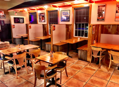 Cozy restaurant interior with wooden tables, chairs, and illuminated booths, featuring framed posters on the walls.