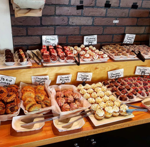 A display of various baked goods, including cupcakes, cookies, and pastries, arranged on a wooden counter.