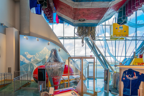 Interior view of a museum featuring boats, nautical equipment, and a backdrop of mountains and clouds.