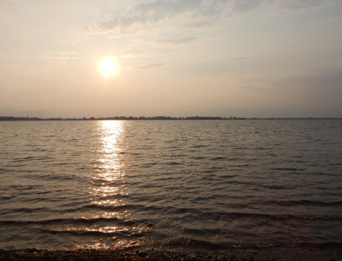 A serene sunset over a calm lake, with soft waves reflecting the golden light and a distant shoreline.