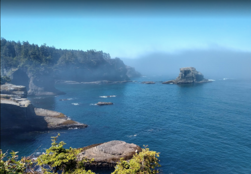 A serene coastal view with rocky cliffs, clear blue water, and a misty horizon under a bright sky.