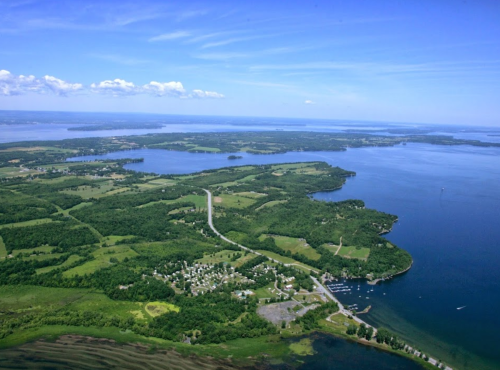 Aerial view of a lush green landscape with lakes, rivers, and a small town along the shoreline under a clear blue sky.