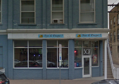 Exterior of a blue building with a sign that reads "Tea & Crepe!" and large windows showcasing the entrance.