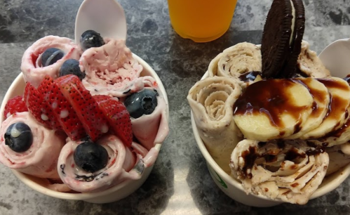 Two bowls of rolled ice cream: one with strawberries and blueberries, the other with bananas, Oreos, and chocolate sauce.