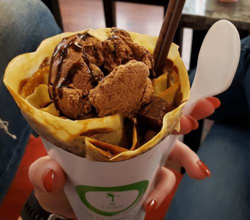 A hand holding a cup filled with chocolate ice cream, drizzled with chocolate sauce, and topped with a wafer.