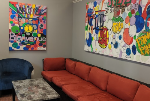 A cozy lounge area with a blue chair, red sofa, and colorful abstract artwork on the walls.