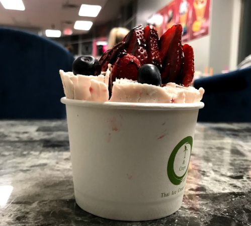 A cup of rolled ice cream topped with fresh strawberries and blueberries on a marble table.