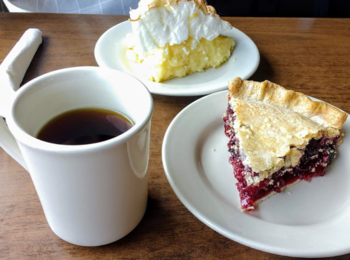 A cup of coffee beside a slice of berry pie and a serving of meringue dessert on white plates.