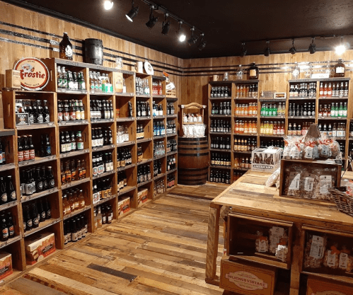 A cozy store interior with wooden shelves filled with various bottled beverages and snacks, featuring rustic decor.