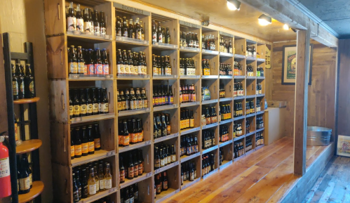 A wooden shelf filled with various bottles of soda, arranged neatly in a cozy, rustic space.