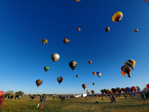 A vibrant sky filled with colorful hot air balloons above a crowd on a grassy field.