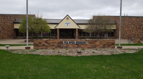 Front view of the W.H. Over Museum, featuring a brick facade and landscaped area with grass and trees.