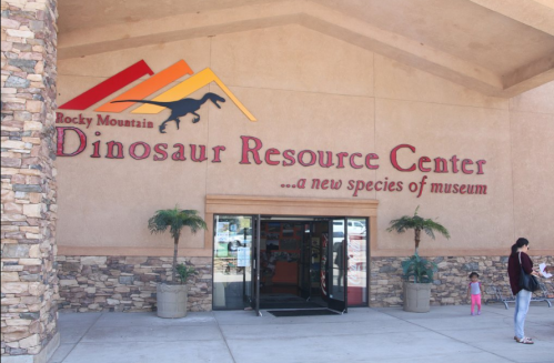 Sign for the Rocky Mountain Dinosaur Resource Center, featuring a dinosaur silhouette and palm trees outside the entrance.