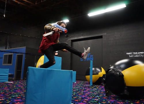 A person jumps over a blue obstacle in a colorful indoor play area with inflatable targets.