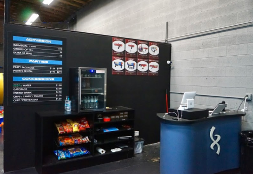Interior of a concession area with a menu board, snacks, and a checkout counter in a recreational facility.
