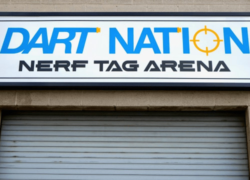 Sign for "DART NATION" Nerf Tag Arena, featuring bold blue and orange letters above a closed garage door.