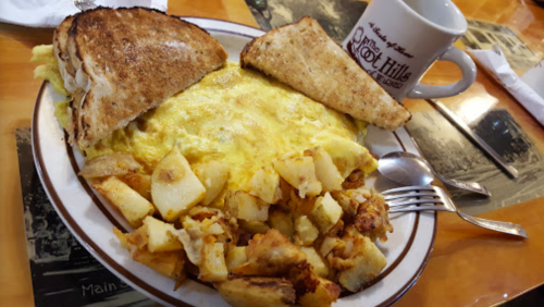 A plate with an omelette, seasoned potatoes, and two slices of toasted bread, alongside a coffee mug.