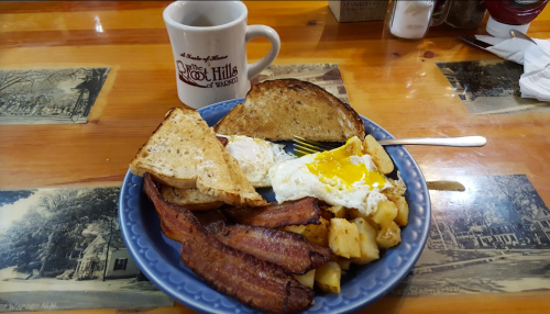 A plate of breakfast with eggs, bacon, toast, and potatoes, alongside a coffee mug on a wooden table.