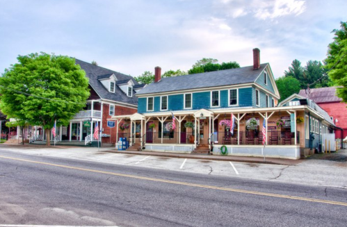 Charming small-town street with colorful buildings, American flags, and lush green trees lining the road.