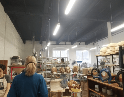 A bakery interior with people working, shelves of bread, and bright overhead lights.