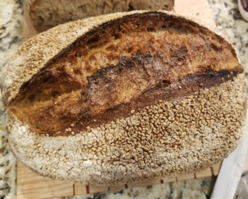A freshly baked loaf of bread with a golden-brown crust and a textured, sesame seed-covered surface.