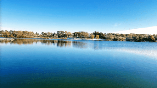 A serene lake reflecting a clear blue sky, surrounded by trees and a peaceful landscape.