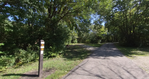A pathway splits in a wooded area, marked by a post with numbers 1 and 2, surrounded by lush greenery.