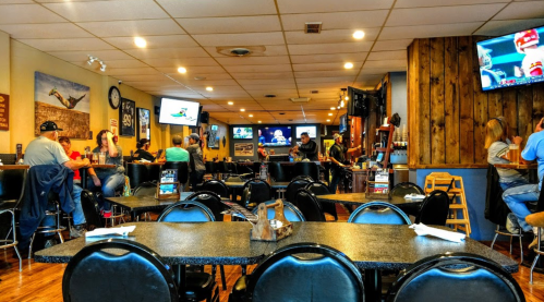 A casual restaurant interior with tables, a bar area, and multiple TVs showing sports. Patrons are enjoying their meals.