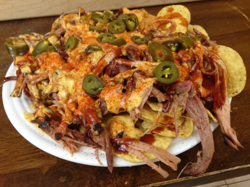 A plate of nachos topped with pulled pork, cheese, jalapeños, and spices on a wooden table.