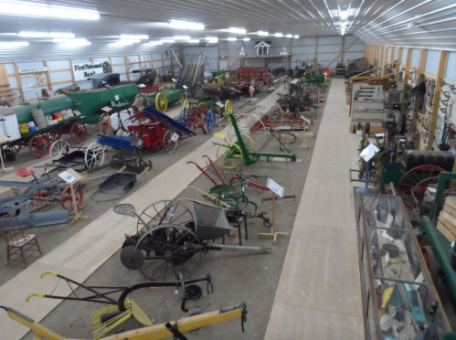 A wide view of a museum displaying various vintage farming tools and equipment in a spacious, well-lit interior.